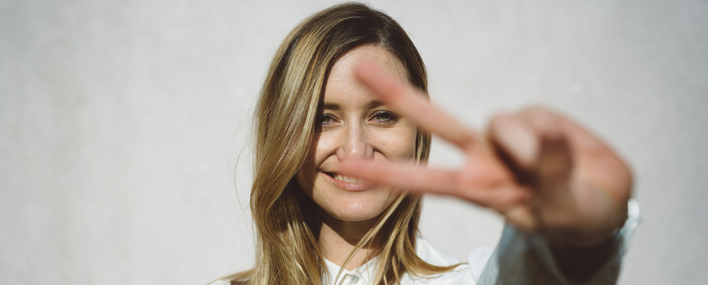Smiling woman holding up a peace sign, symbolising accountability coaching, focus and strong goal setting strategies