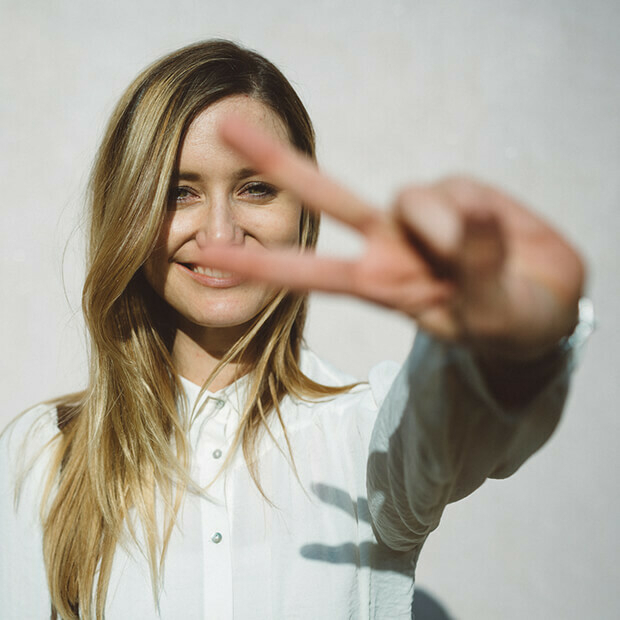 Smiling woman holding up a peace sign, symbolising accountability coaching, focus and strong goal setting strategies