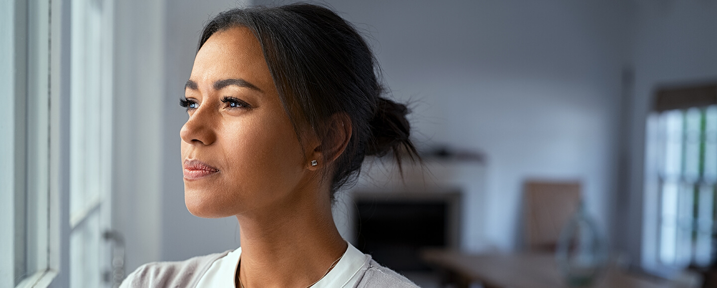 A woman gazing out of a window in quiet reflection, representing midlife clarity and empowered decision-making.