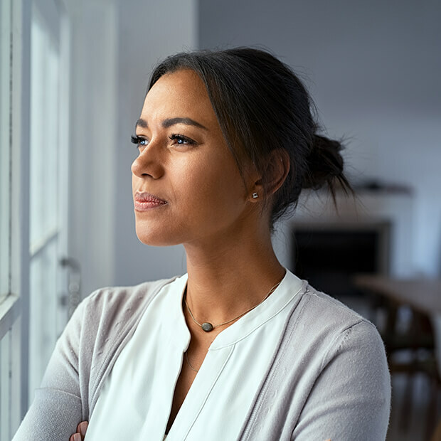 A woman gazing out of a window in quiet reflection, representing midlife clarity and empowered decision-making.